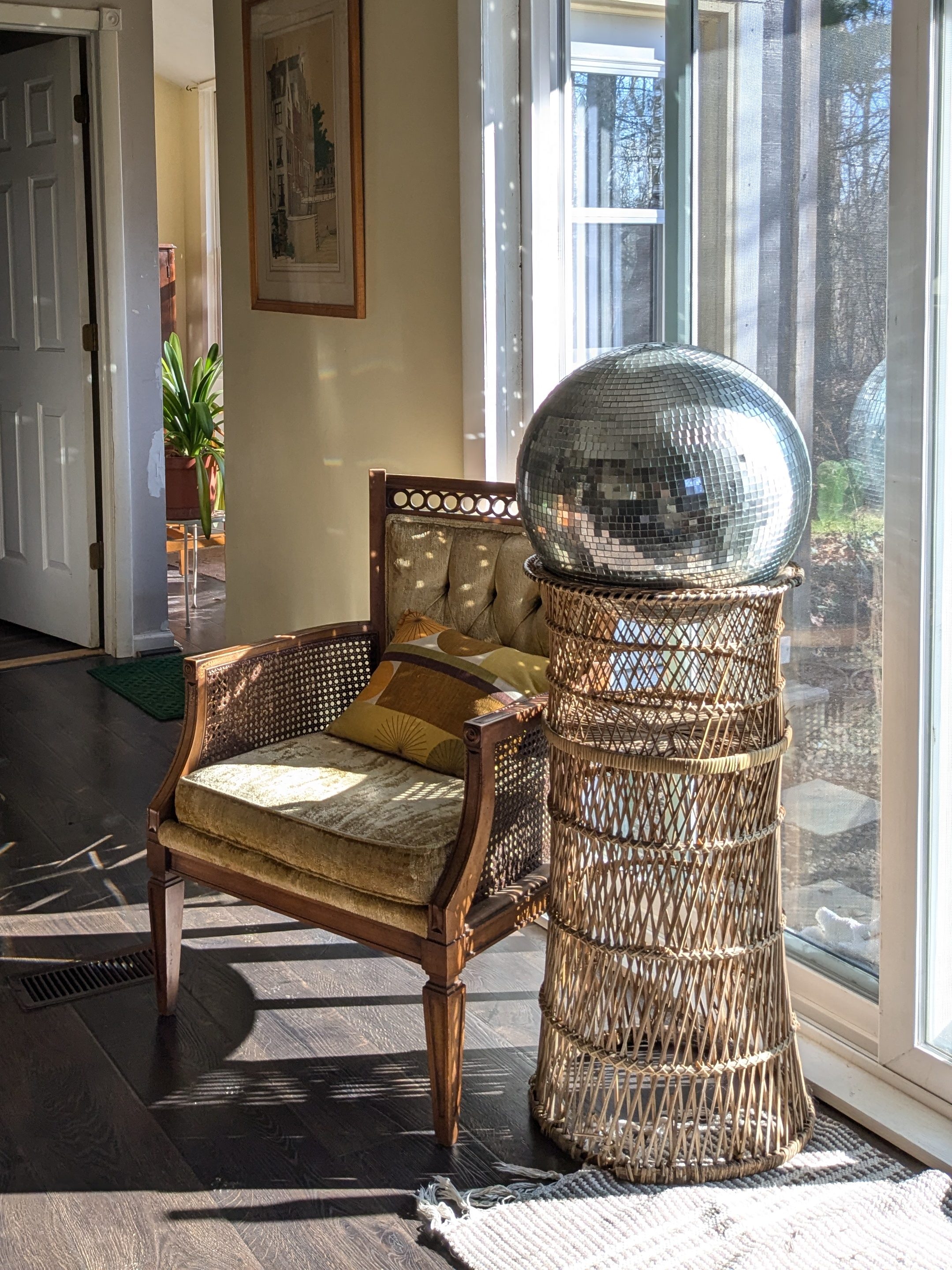 mirror ball on a wicker stand next to a green, vintage velvet chair