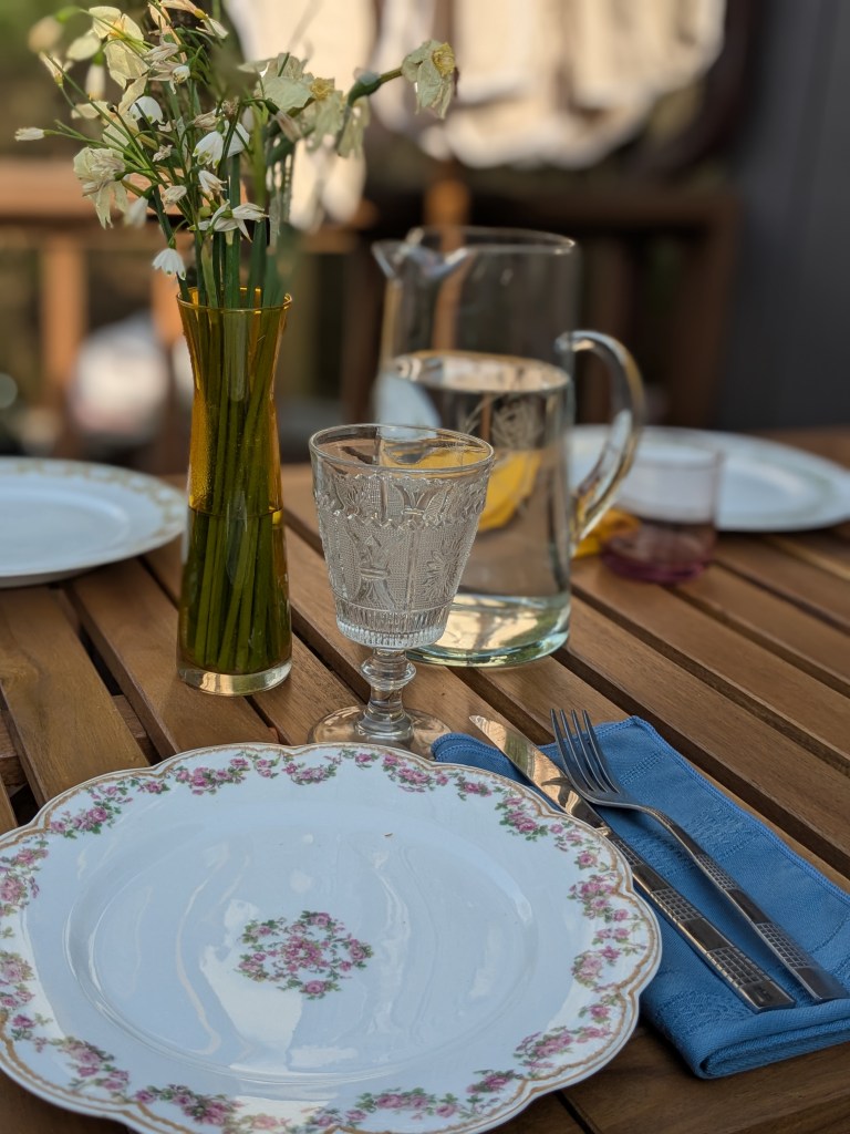 a vintage table setting with a plate, silverware, vase with flowers, and glass pitcher